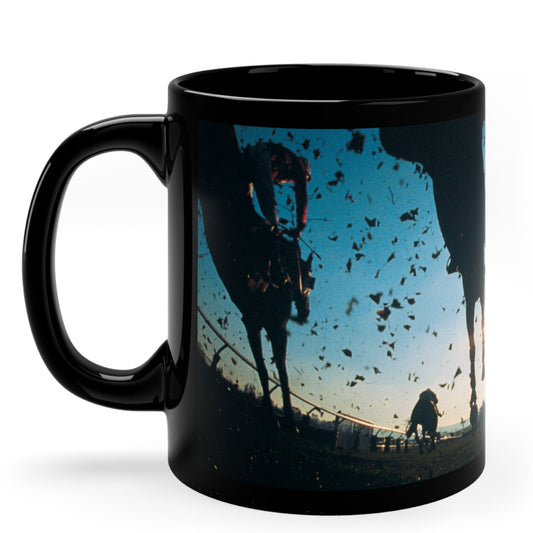 Dramatic black ceramic mug featuring a low-angle ground view of racing horses kicking up dirt at sunrise. 11oz, microwave and dishwasher safe.